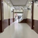 Lamri nhựa giả gỗ Nano NA29 vân walnut nâu đậm bề mặt phẳng bản rộng wainscoting bọc cột cả 2 bên hành lang vách cầu thang tường vàng kem sàn gạch ceramic nhà phố TP.HCM