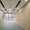 Vách lam sóng 3S09A màu vân gỗ oak sáng ốp tường văn phòng mặt bằng kinh doanh phong cách Modern Office trần viền đen sàn thảm xám TP.HCM